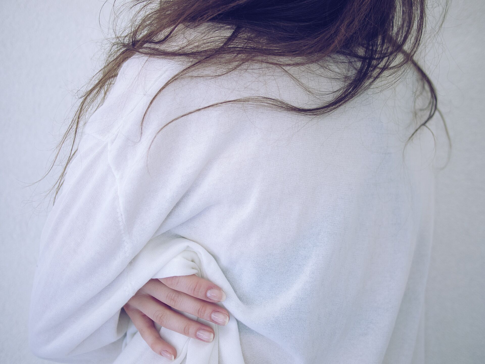 Detailaufnahme einer Person in einem weißen Pullover, deren Hand locker den Stoff greift.