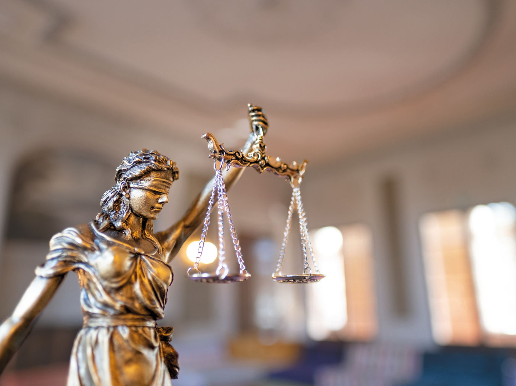 Nahaufnahme einer Justitia-Statue mit Waage, Symbol für Gerechtigkeit und Rechtsprechung, vor unscharfem Hintergrund.