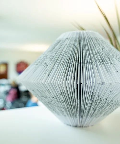 Gefaltetes Buchobjekt in Diamantform dient als dekoratives Element in einem hellen Raum.