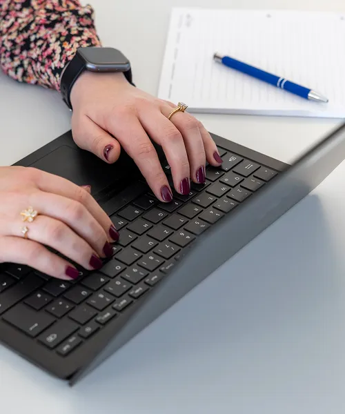 Nahaufnahme von Händen mit dunkel lackierten Nägeln, die auf einer Laptop-Tastatur tippen.