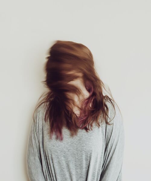 Person mit langem Haar bewegt den Kopf schnell, wodurch das Gesicht verschwommen und verdeckt erscheint.
