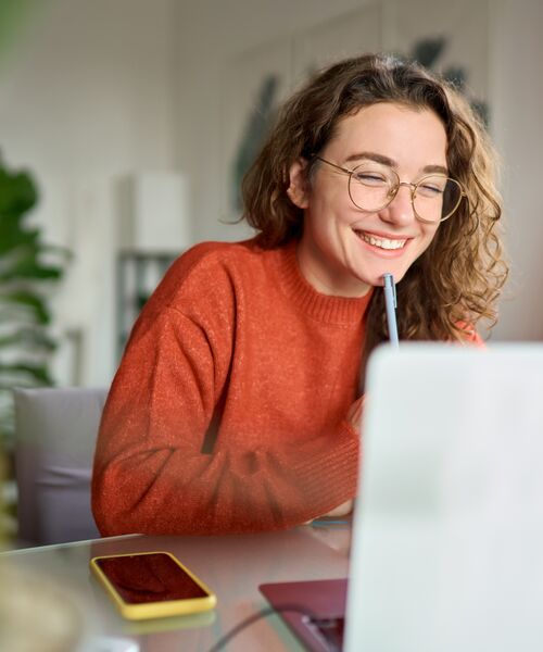 Ein heller Tisch mit orangefarbenen Tulpen, einer Lampe und kleinen bunten Ringen neben einem cremefarbenen Ledersessel.