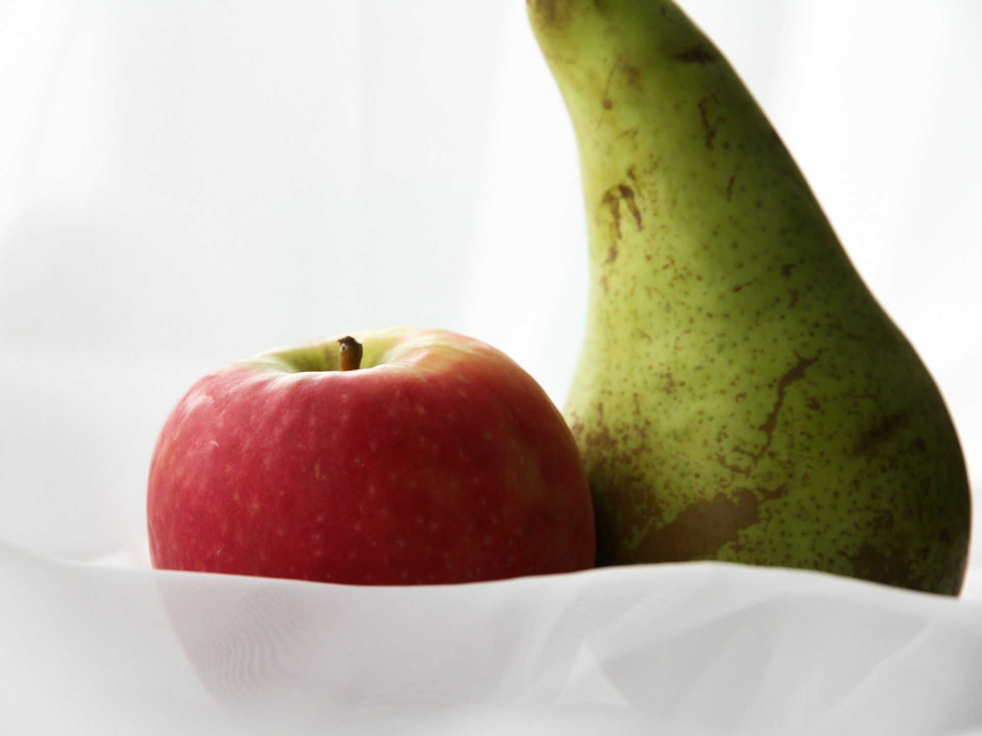 Nahaufnahme eines roten Apfels und einer grünen Birne auf weißem Untergrund, Symbol für gesunde Ernährung.