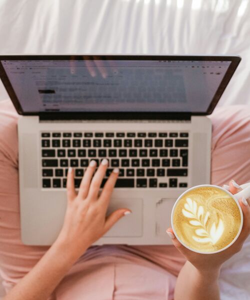 Person arbeitet am Laptop und hält eine Tasse Kaffee mit Latte-Art, Symbol für konzentriertes und entspanntes Arbeiten.