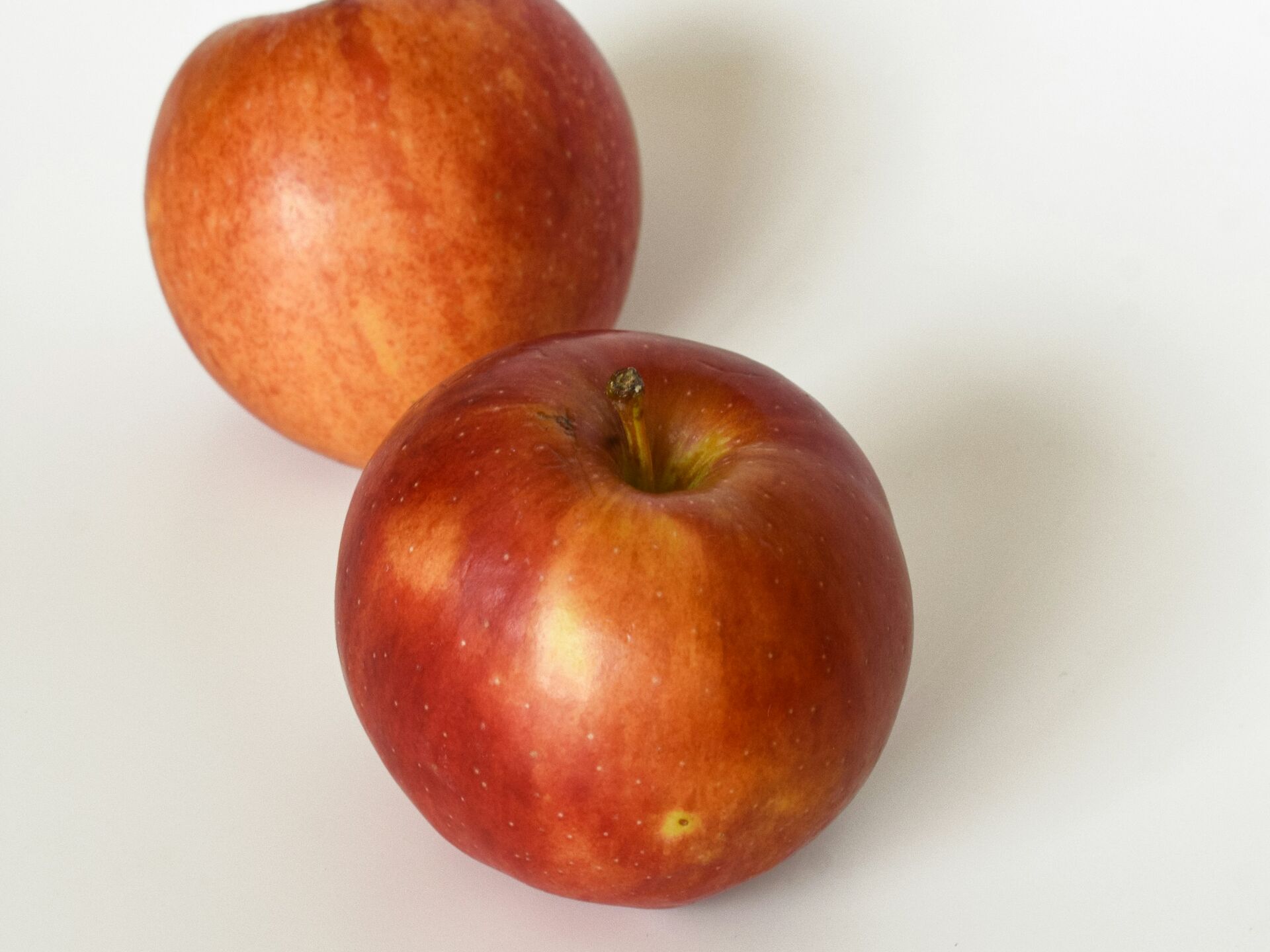 Zwei rote Äpfel liegen auf einer weißen Fläche, minimalistisch arrangiert.