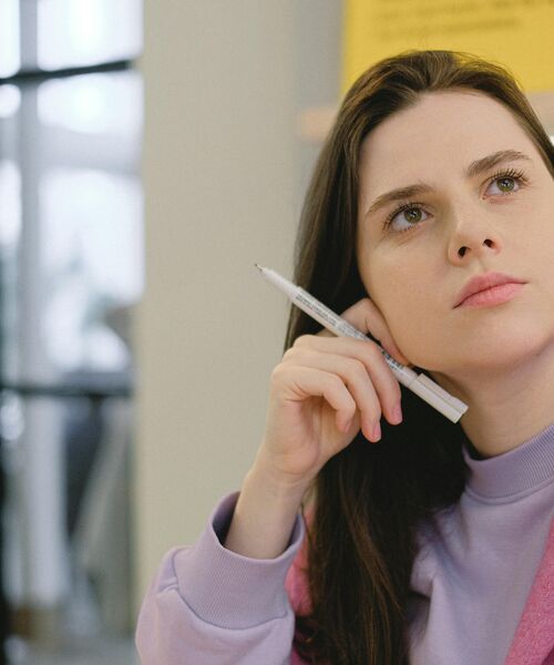 Nachdenkliche junge Frau hält einen Stift und blickt konzentriert in die Ferne, Symbol für Planung oder kreative Ideenfindung.