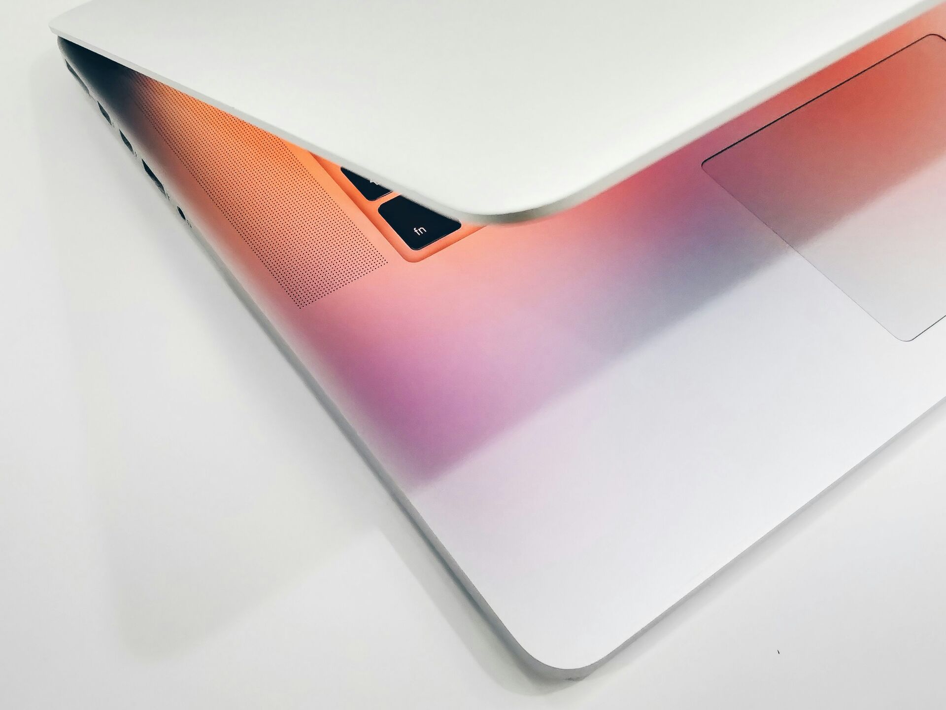 Teilweise geschlossener Laptop auf weißem Hintergrund, beleuchtet von warmem, farbigem Licht.