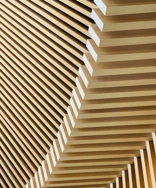 Architektonisches Detail einer Decke aus parallel verlaufenden Holzlamellen mit geometrischer Struktur.