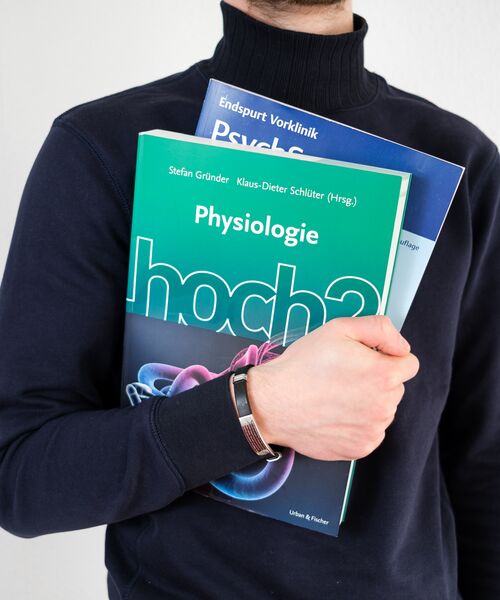Person hält mehrere medizinische Lehrbücher, darunter eines mit dem Titel „Physiologie“.