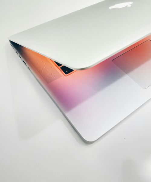 Teilweise geschlossener Laptop auf weißem Hintergrund, beleuchtet von warmem, farbigem Licht.