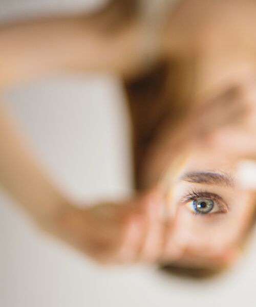 Nahaufnahme eines Auges, das durch eine unscharfe Fläche hindurch sichtbar ist. Der Fokus liegt auf dem Auge, während der Rest des Bildes weich verschwimmt.