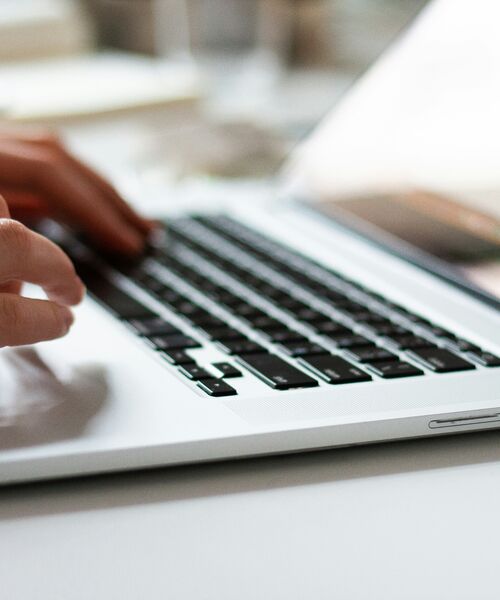 Nahaufnahme einer Person, die auf einer Laptop-Tastatur tippt, mit Fokus auf den Händen und den Tasten.