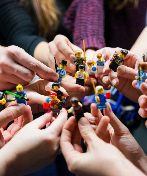 Mehrere Hände halten bunte Spielfiguren zusammen, die in der Mitte einander zugewandt sind.
