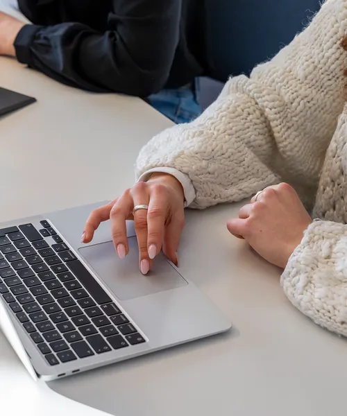 Nahaufnahme einer Person in heller Strickkleidung, die an einem Laptop arbeitet.