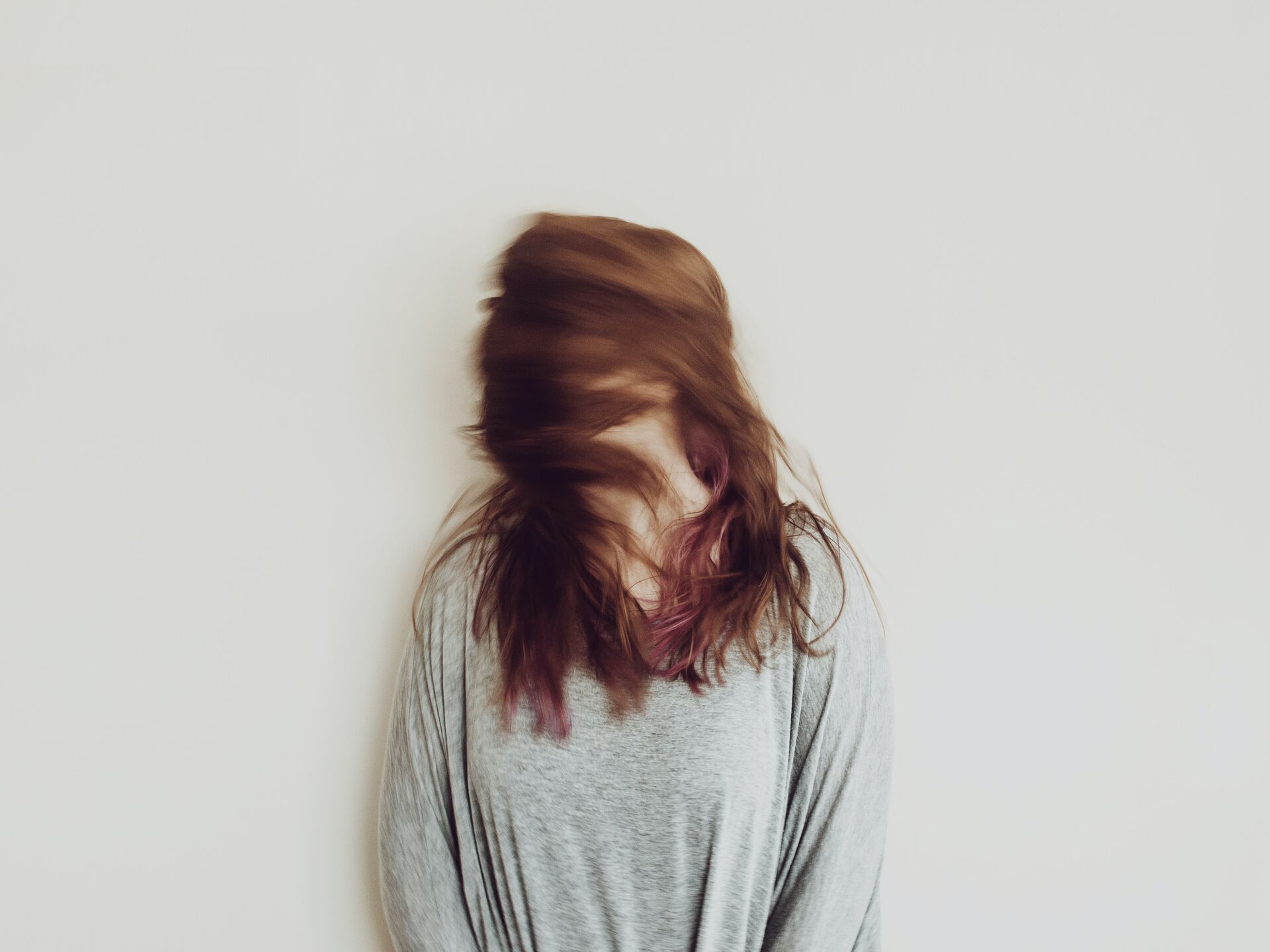 Person mit langem Haar bewegt den Kopf schnell, wodurch das Gesicht verschwommen und verdeckt erscheint.