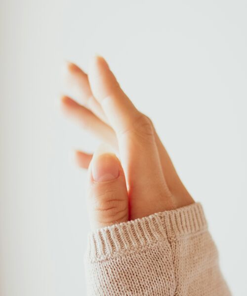 Eine Hand in einem hellen Pullover ist sanft angehoben und wird von warmem Licht beleuchtet.
