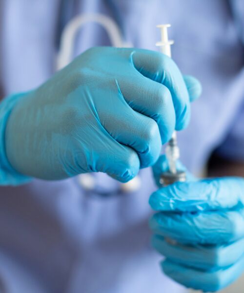 Eine medizinische Fachkraft mit blauen Handschuhen zieht eine Flüssigkeit mit einer Spritze auf.