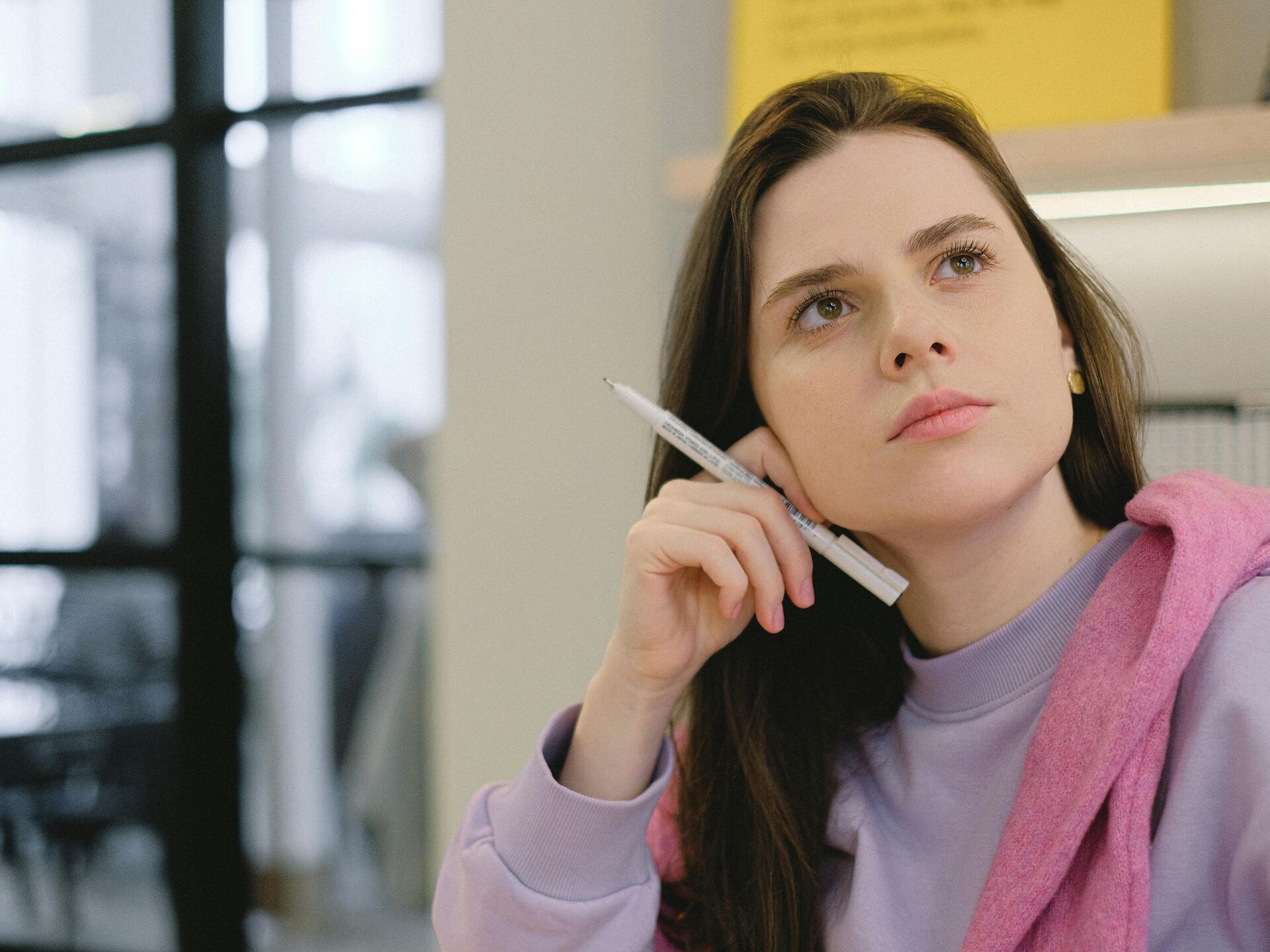 Nachdenkliche junge Frau hält einen Stift und blickt konzentriert in die Ferne, Symbol für Planung oder kreative Ideenfindung.