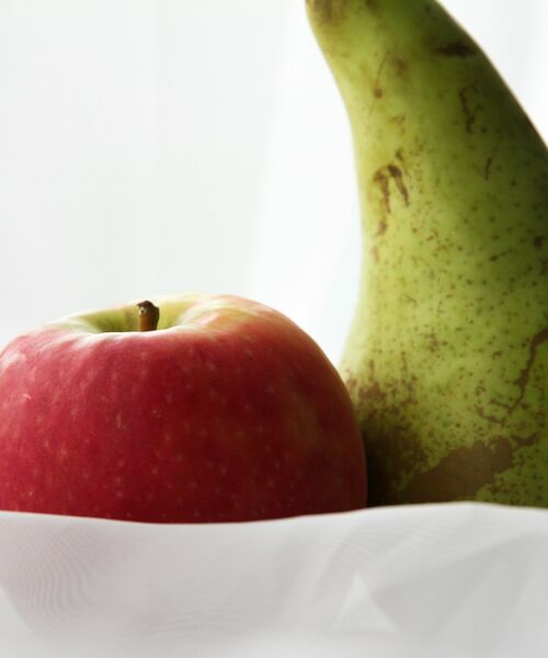 Nahaufnahme eines roten Apfels und einer grünen Birne auf weißem Untergrund, Symbol für gesunde Ernährung.