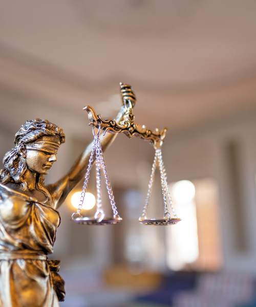 Nahaufnahme einer Justitia-Statue mit Waage, Symbol für Gerechtigkeit und Rechtsprechung, vor unscharfem Hintergrund.