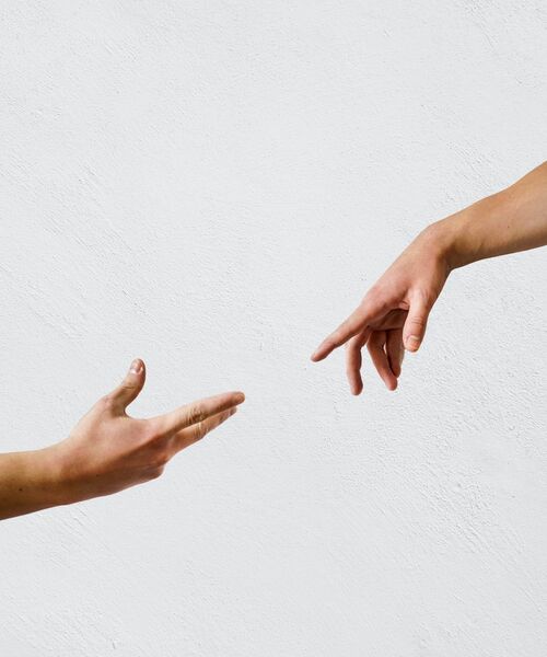 Zwei Hände strecken sich aufeinander zu, vor hellem Hintergrund – Symbol für Verbindung und Unterstützung.