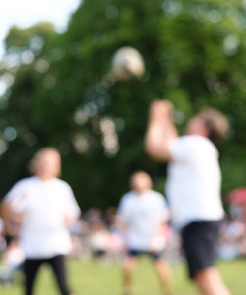 Unscharfes Foto von Personen, die im Freien Ball spielen, mit grünem Hintergrund und sommerlicher Atmosphäre.