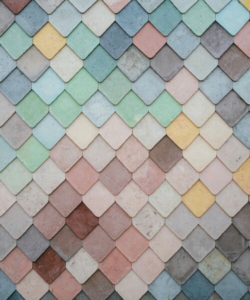 Bunte Wand aus überlappenden, rautenförmigen Fliesen in Pastellfarben.