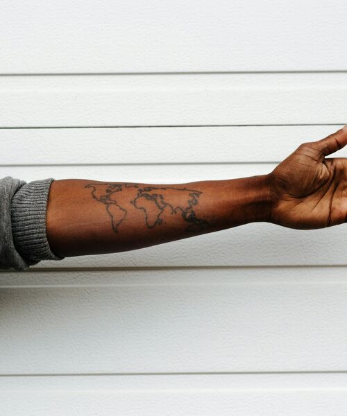 Ausgestreckter Arm mit einer Tätowierung der Weltkarte auf dem Unterarm vor weißem Hintergrund.