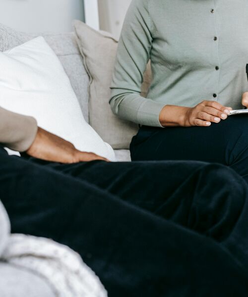 Zwei Personen sitzen auf einem Sofa, eine Person hält ein Tablet oder Notizbuch in den Händen.