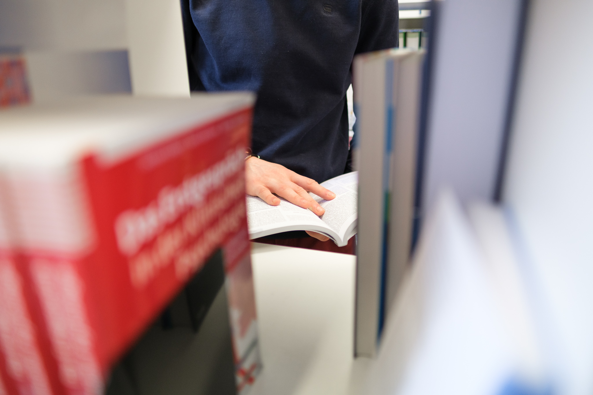 Person blättert in einem aufgeschlagenen Buch zwischen Bücherregalen in einer Bibliothek.
